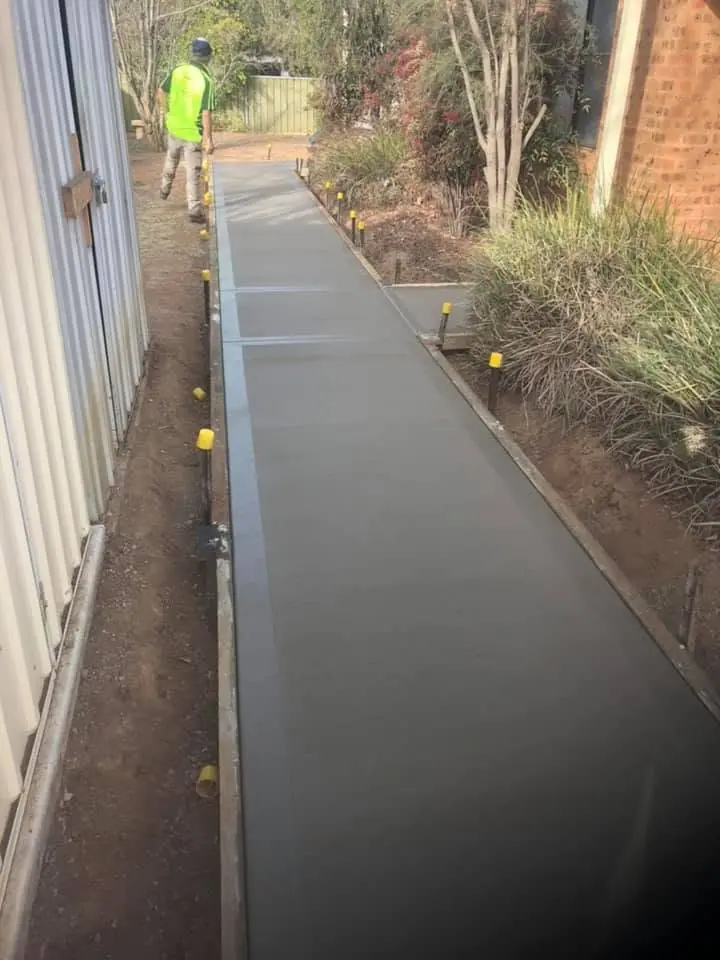 Worker near freshly finished concrete paving beside a brick building